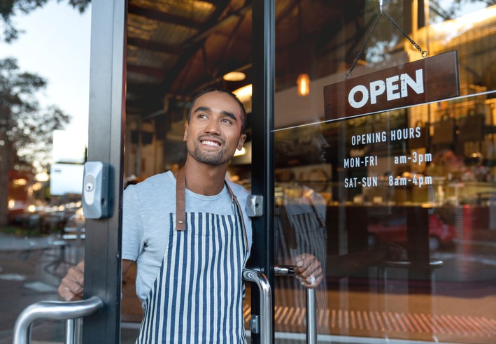 Portrait of a happy waiter opening on the doors at a cafe and smiling - small business concepts
